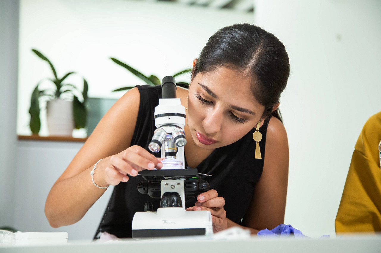 A woman of color looking through a microscope.